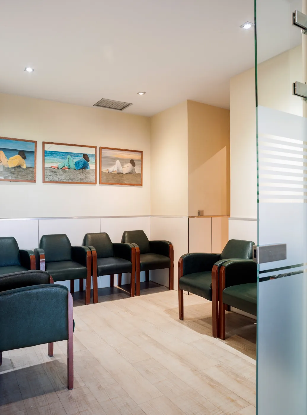 Sala de espera de la consulta — sillones tapizados, cuadros de mar, suelo de madera clara