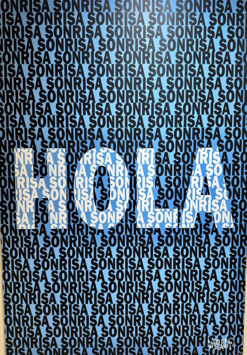 Obra «Sonrisa» firmada por Varela — la palabra SONRISA repetida sobre fondo azul, expuesta en la consulta
